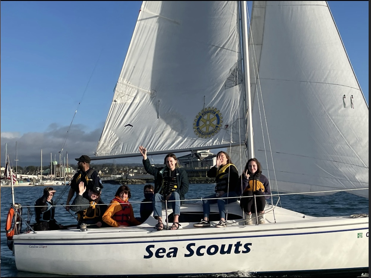 Group of Sea Scouts waving aboard a sailboat that says Sea Scouts on the side